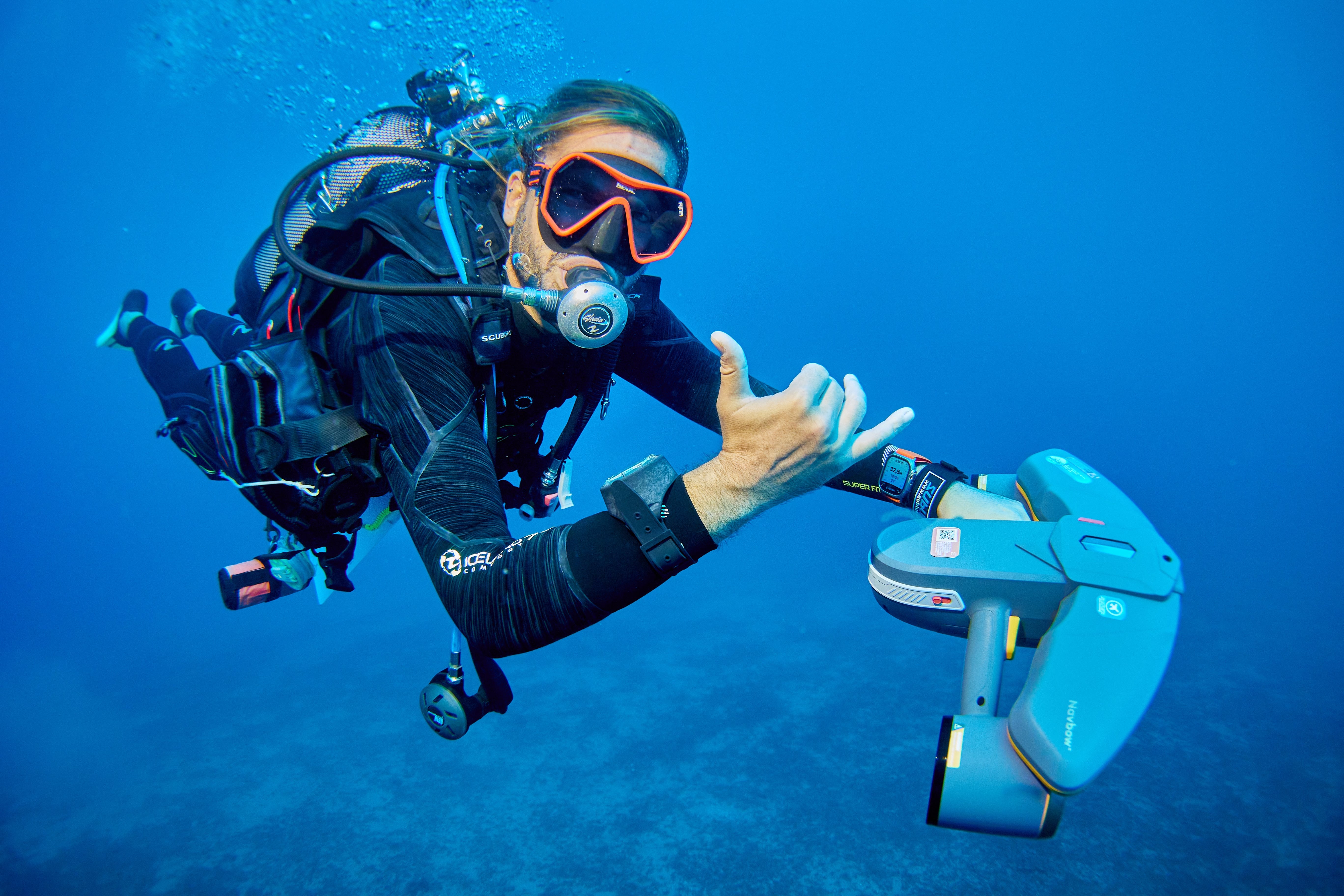 plongeur qui fait un signe de la main avec un sea scooter sublue